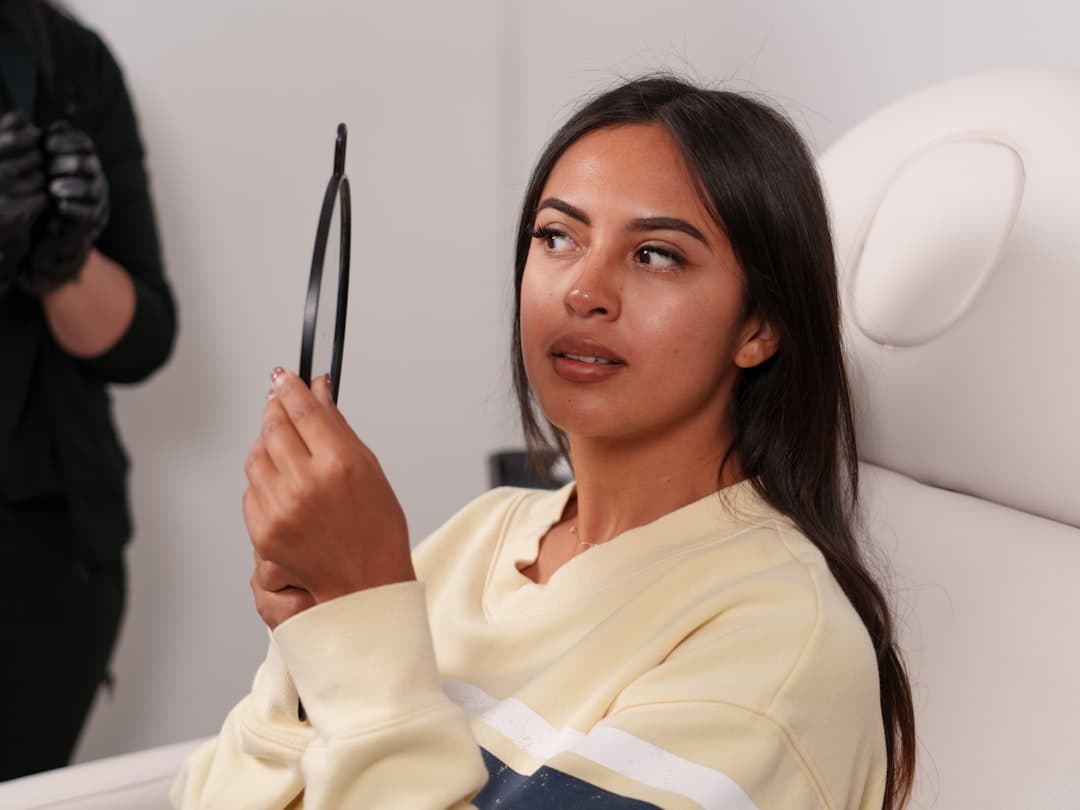 A patient holding a mirror during a treatment consultation at a med spa
