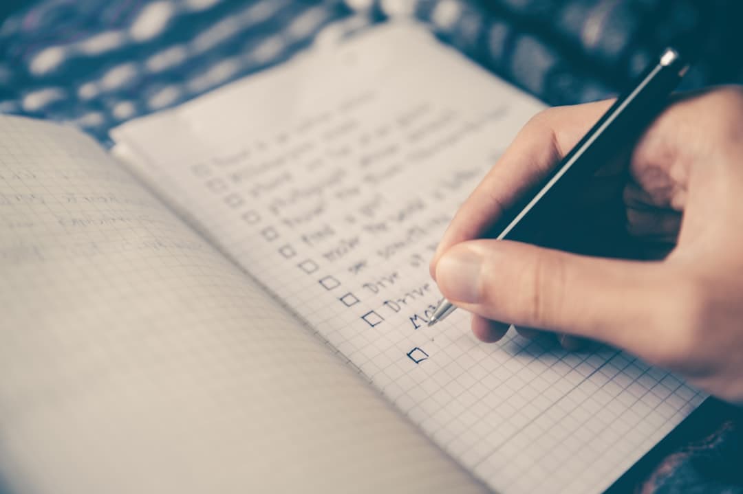 A hand writing a short list by hand in a gridded notebook